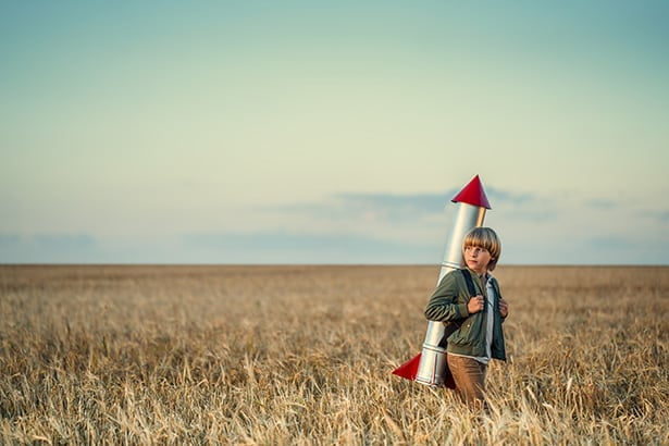 Un garçon se reflète alors qu'il se tient dans un champ avec une fusée jouet pour montrer le succès d'un développement personnalisé d'applications