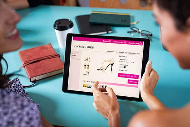 Deux femmes utilisant un iPad pour parcourir des chaussures sur un site Web e-commerce