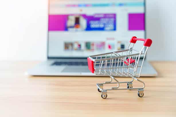 Un caddie de jouets posé sur une table en bois devant un ordinateur portable, soulignant le potentiel du commerce électronique