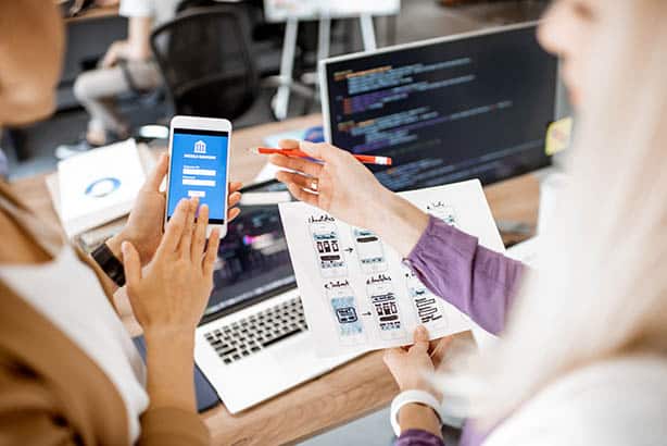 Deux femmes regardant un smartphone dans un bureau, discutant d'une application personnalisée développée par une entreprise