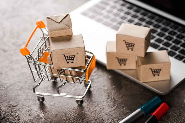 un panier d'achat et des boîtes à côté d'un ordinateur portable pour parler d'une migration de Shopify vers Magento